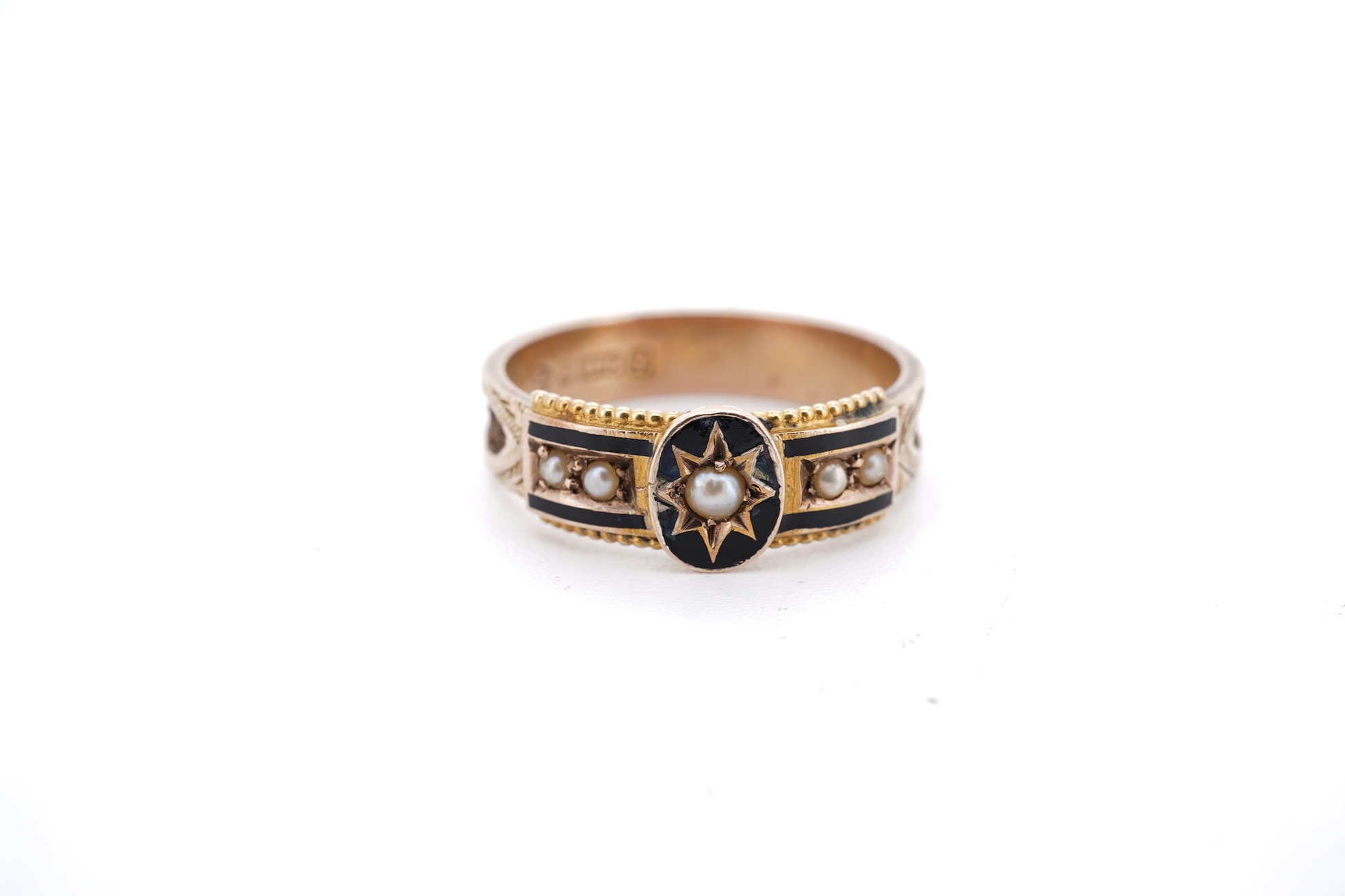 A George V 9ct gold, black enamel and seed pearl set mourning ring, the shank with panels of plaited hair, size O, gross weight 2.5 grams.